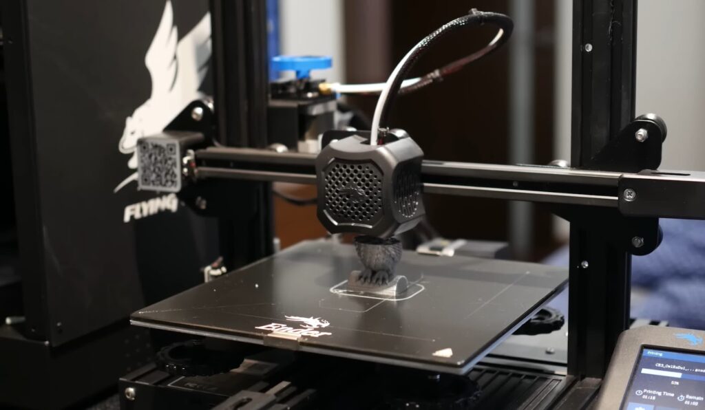 A black filament 3D printer creating a gray object